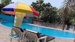 A swimming pool with lounge chairs and a colorful umbrella. - Sukh Sagar Resort (Kaliganj)