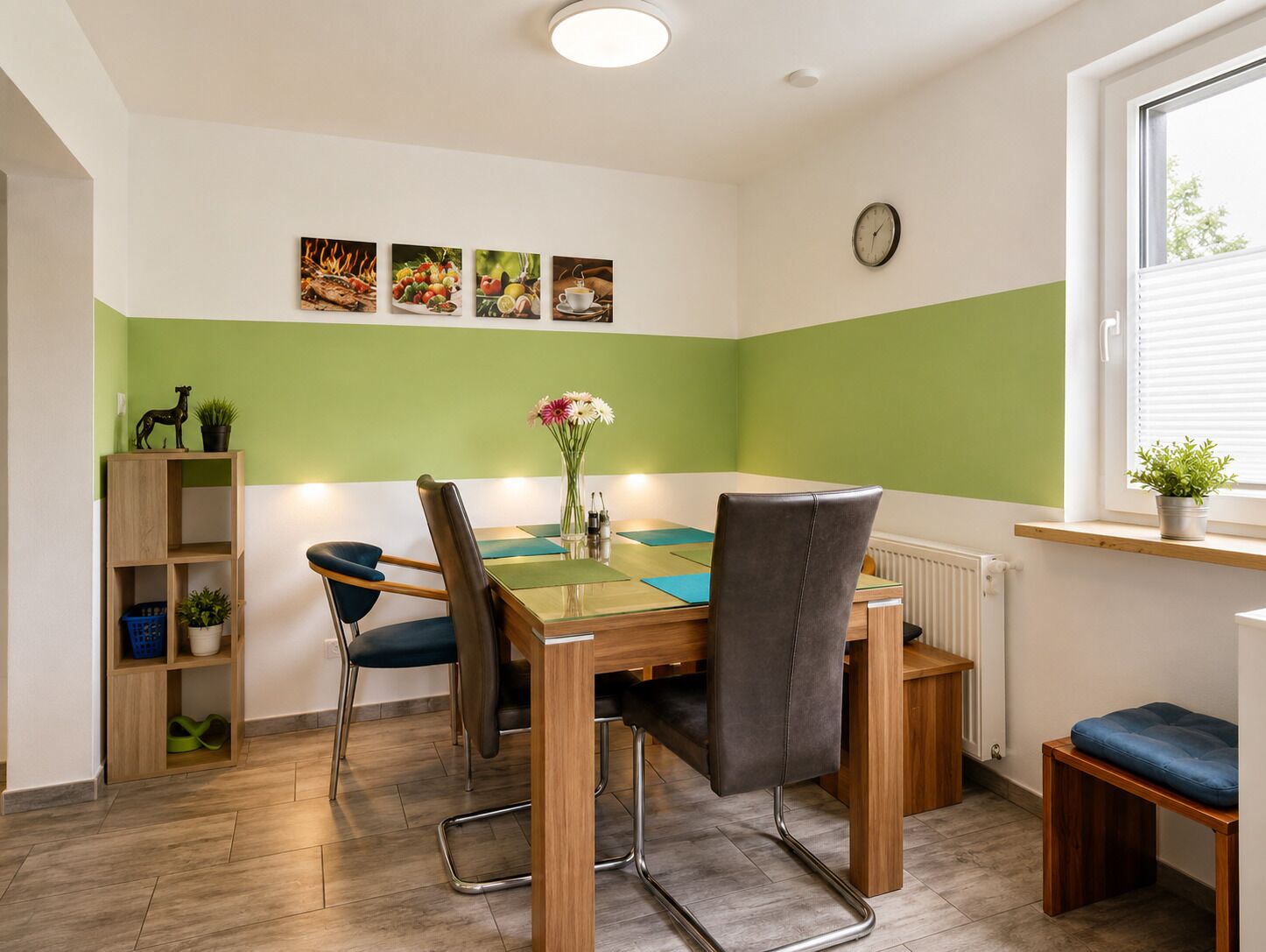 A dining area with a wooden table, two chairs, a vase with flowers, and a shelf with items.