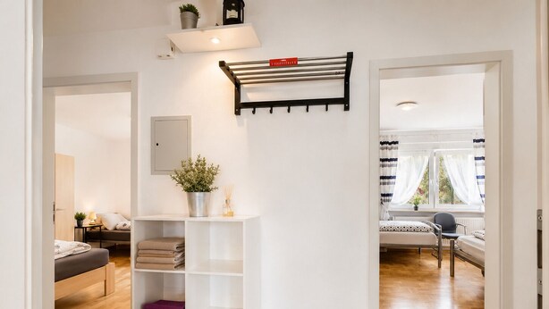 A modern interior with a white wall-mounted shelf, a bed with a headboard, a seating area with a chair, and a window with curtains.