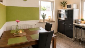 A compact kitchen with a dining table, chairs, a microwave, oven, and a small bar area.