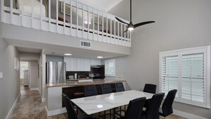 A modern kitchen with a central island, a dining area with a white table and black chairs, and a balcony with white railings.