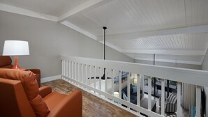 A modern interior with a high ceiling, a white railing, and a view of an outdoor patio area.