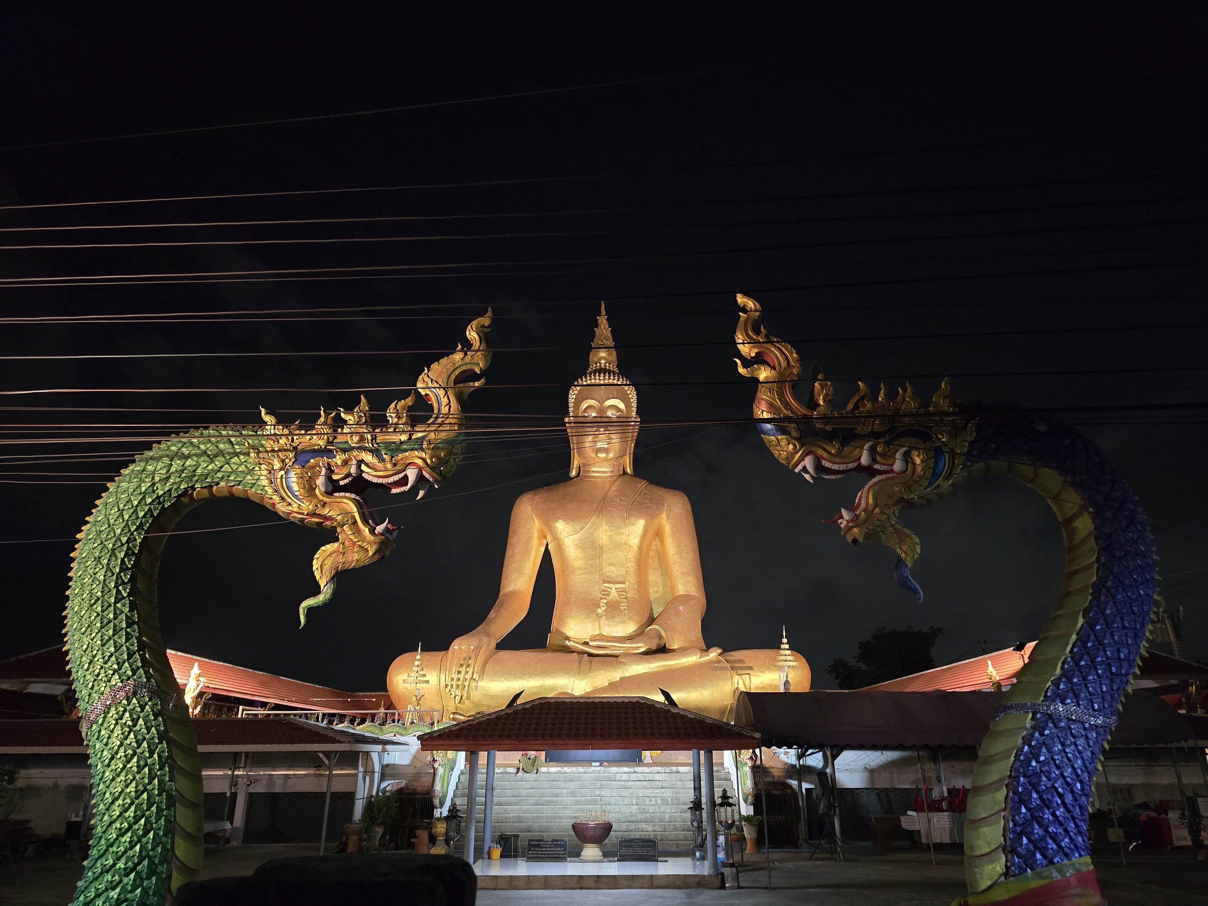 Eine große goldene Buddha-Statue mit Drachen links und rechts, vor einem dunklen Nachthimmel.
