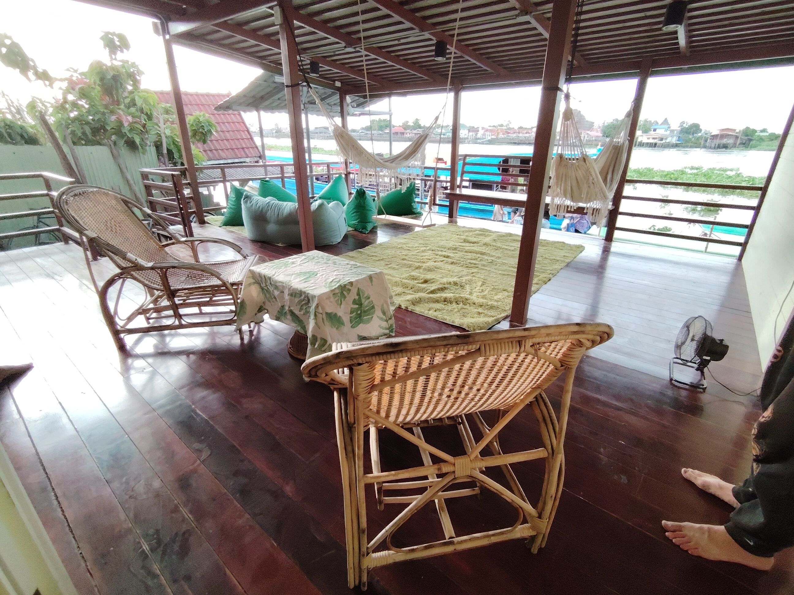 A covered outdoor seating area with wicker furniture, a table with a leaf-patterned tablecloth, and a view of the water.