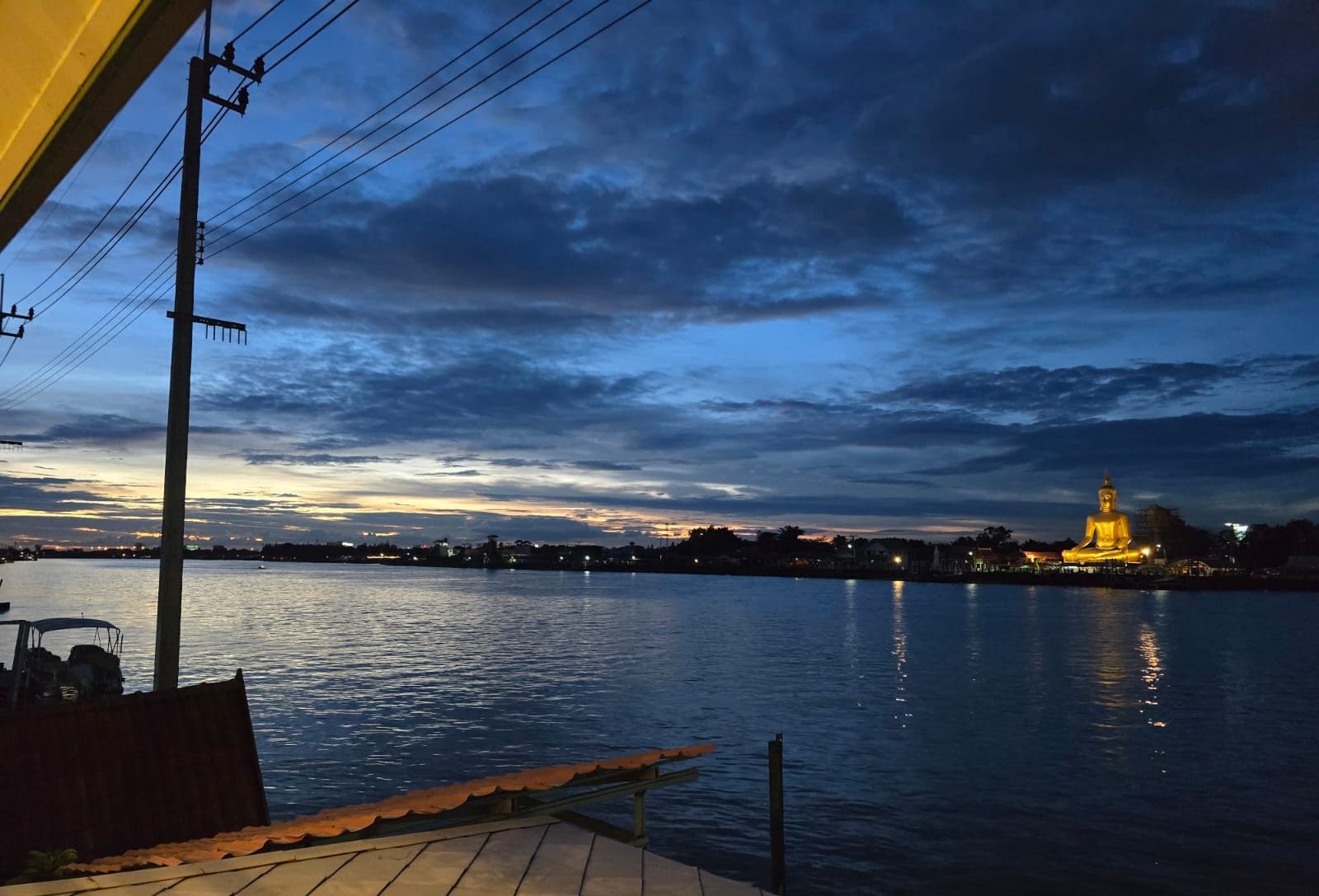 A waterfront view with a large golden Buddha statue illuminated against a twilight sky.