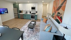 A modern apartment with a kitchen, dining area, and living room. It includes a flat-screen TV, a sofa, and a patterned rug.