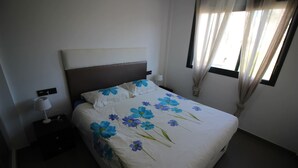 Un letto rifatto con cura, una coperta a fiori, una lampada da comodino e una finestra con tende.