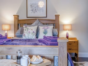 A neatly made bed with purple towels, a bedside table with a tray of food and drinks, and a wooden headboard. - The Old Cottage - UK49169 (Beadnell)