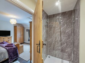 A modern bathroom with a glass shower enclosure, a wooden door, and a visible bathtub. - The Old Cottage - UK49169 (Beadnell)