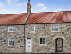 A stone building with a red-tiled roof, a white door, and multiple windows. - The Old Cottage - UK49169 (Beadnell)
