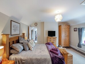A bedroom with a bed, a television, a wardrobe, and a chandelier. - The Old Cottage - UK49169 (Beadnell)