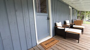 Un porche avec un paillasson, des chaises en osier et une porte.