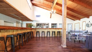 Une pièce spacieuse avec un plancher en bois, un long comptoir-bar avec des tabourets et une table de ping-pong.