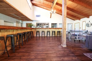 Une pièce spacieuse avec un plancher en bois, un long comptoir-bar avec des tabourets et une table de ping-pong.