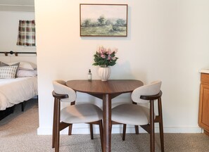 Ein kleiner Essbereich mit einem runden Holztisch, vier Stühlen, einer Blumenvase und einem Bild an der Wand.