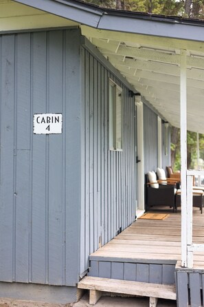 Une cabane portant l’inscription « Cabane 4 », dotée d’un porche couvert et d’un espace extérieur aménagé avec des sièges.