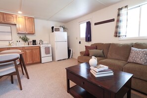 A compact living space with a kitchenette, a dining area, and a seating area with a sofa and a coffee table. - Wilderness West Resort Cabin 4 (Colville)