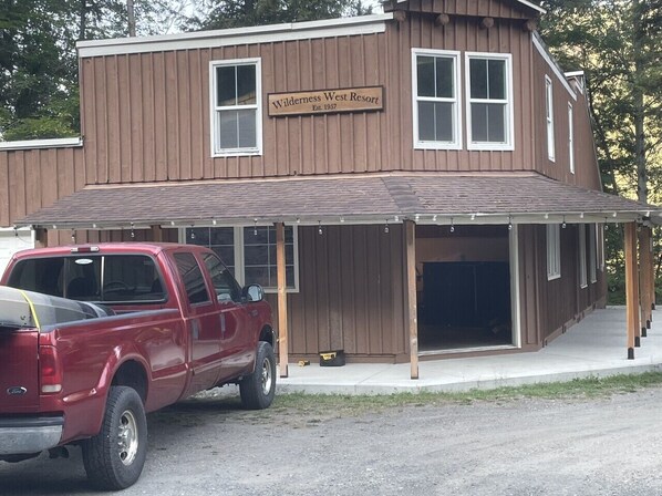 A two-story building with a sign reading 'Wilderness West Resort' and a covered parking area with a red pickup truck parked in front.