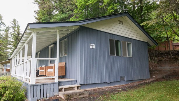 A small cabin with a porch, a sign indicating it is cabin number 5, and a wooden deck with outdoor furniture.