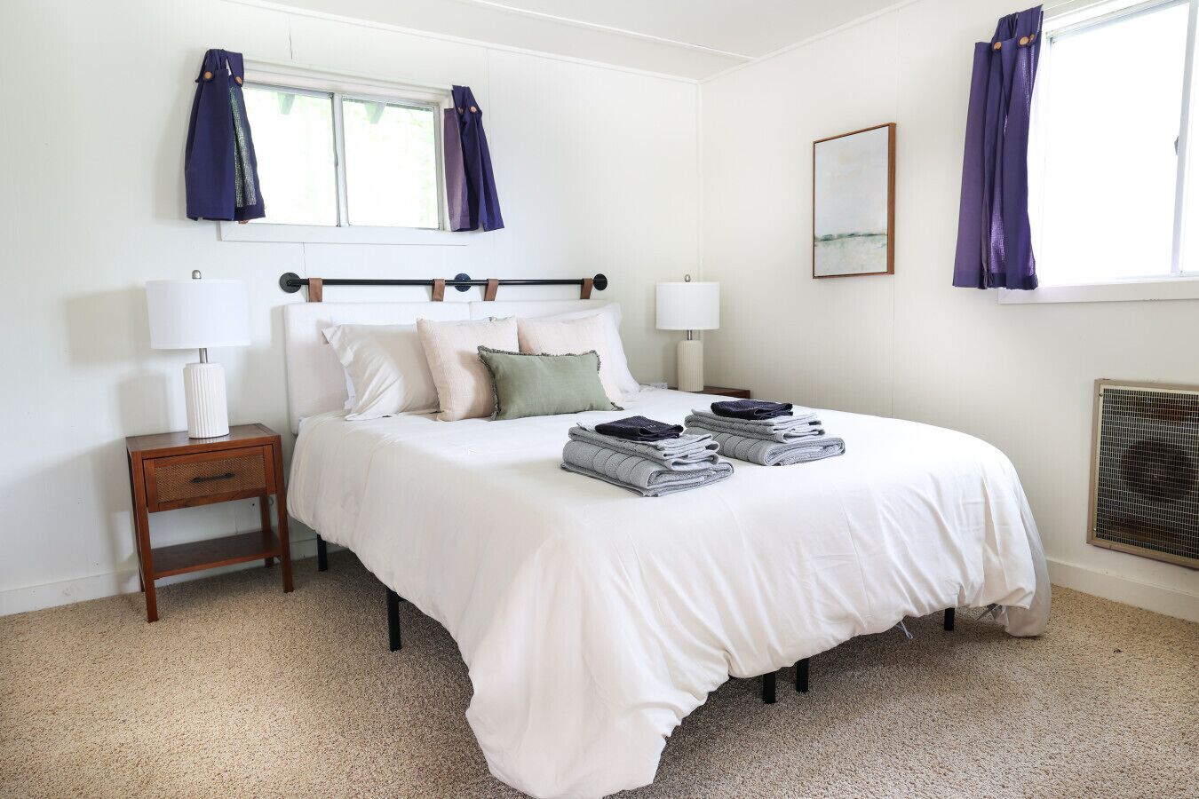 A neatly arranged bedroom with a bed, bedside lamps, a small table, and a window with curtains.