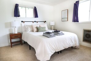 A neatly arranged bedroom with a bed, bedside lamps, a small table, and a window with curtains. - Wilderness West Resort Cabin 5 (Colville)