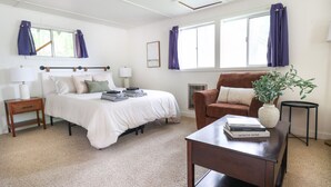 A bedroom with a bed, bedside tables, a chair, a small table with books, and a potted plant.