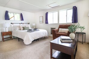 Een slaapkamer met een bed, nachtkastjes, een stoel, een klein tafeltje met boeken en een kamerplant.