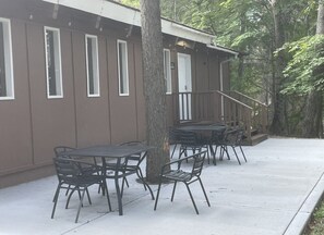 A building with a covered outdoor seating area, including tables and chairs, and a staircase leading to a door.