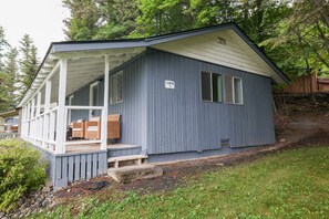 Een klein houten huisje met een veranda, een bordje met het nummer 5 en een terras met tuinmeubilair.