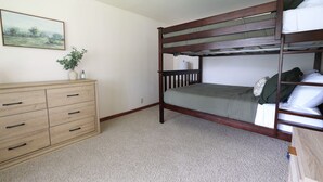 Una cama litera con estructura de madera, un aparador con varios cajones, una planta pequeña en maceta y un cuadro en la pared.