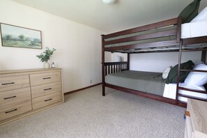 A bunk bed with a wooden frame, a dresser with multiple drawers, a small potted plant, and a framed picture on the wall.