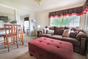 A cozy living room with a brown sofa, a red ottoman, and a dining area with wooden chairs and a table.
