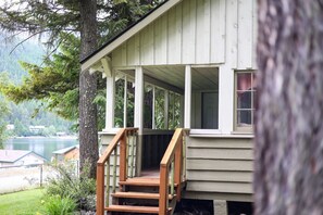 Une cabane en bois dotée d’une véranda, d’un escalier et offrant une vue sur un lac et une forêt.