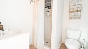 Une salle de bain avec un lavabo blanc, un rideau de douche, des toilettes et une étagère décorative en métal.