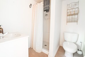 A bathroom with a white sink, a shower curtain, a toilet, and a decorative metal shelf. - Wilderness West Resort Cabin 6 (Colville)