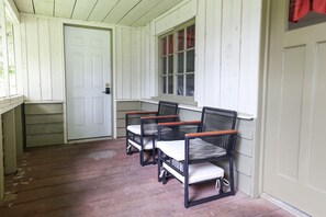 Une véranda avec trois fauteuils en osier et une porte blanche.