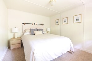 A neatly arranged bedroom with a large bed, two bedside tables with lamps, and three framed pictures on the wall. - Wilderness West Resort Cabin 7 (Colville)
