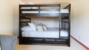 Uma cama beliche com estrutura de madeira, roupa de cama branca e uma gaveta pequena para guardar objetos.