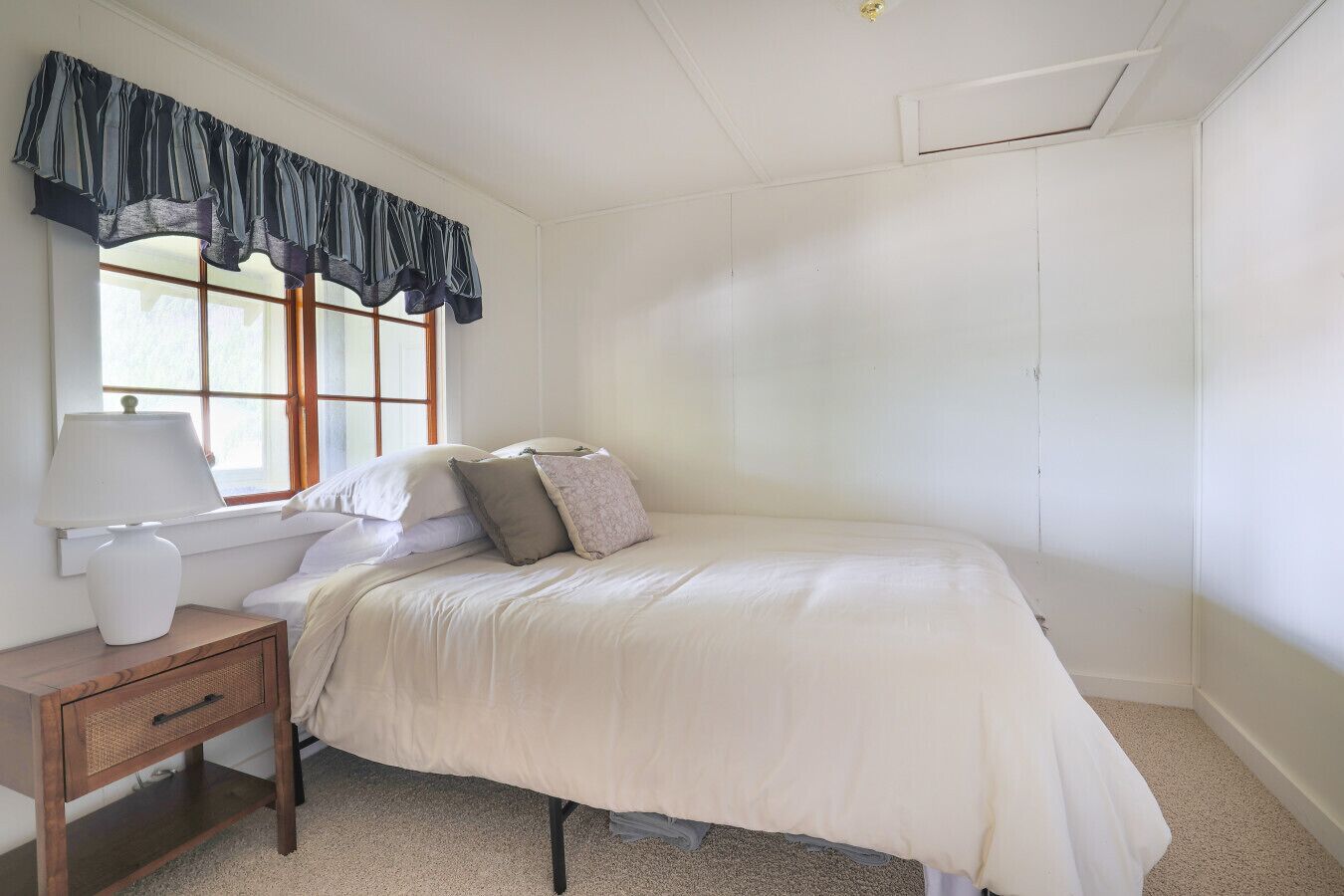 Quarto com cama, mesa de cabeceira, luminária e janela com cortina.