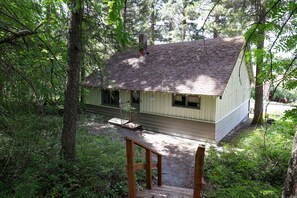 A cabin with a wooden deck, surrounded by dense forest. - Wilderness West Resort Cabin 7 (Colville)