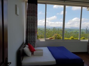 Quarto com uma cama, janela com vista para vegetação e montanhas, e cortina.