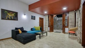 A living room with a sofa, a coffee table, and a chair. There is a door leading to a balcony with a view of a stone wall and a white fence. - Daynish Rock Bungalow (Hatton)