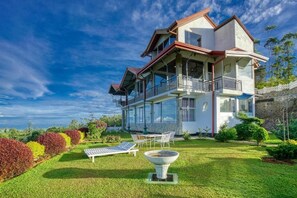 A two-story house with a balcony, a lawn, and a garden.