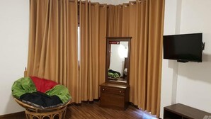 A room with wooden flooring, a television mounted on the wall, a small wooden dresser, and a wicker chair with a colorful cushion. - Daynish Rock Bungalow (Hatton)