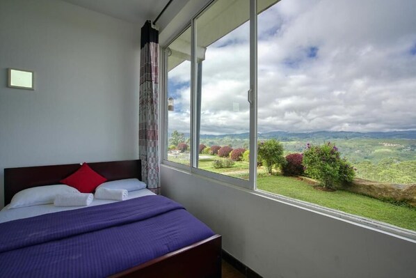 A bedroom with a large window offering a view of a green landscape and hills.