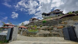 A hillside property with multiple houses, a stone retaining wall, and a paved driveway leading to a gated entrance. - Daynish Rock Bungalow (Hatton)