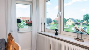 A room with a large window, a radiator, a wooden chair, and a small table with a lamp and flowers.