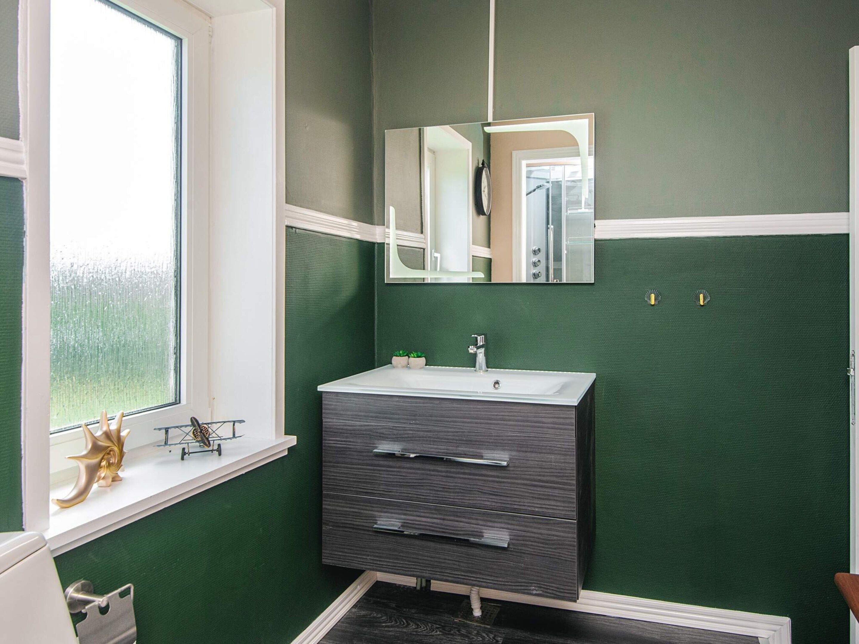 Een badkamer met een raam, een wastafel, een spiegel en een kast.