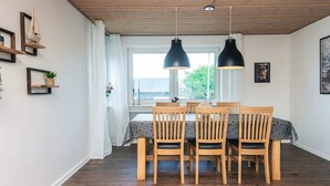 A dining area with a wooden table and chairs, pendant lights, and a view through a window.