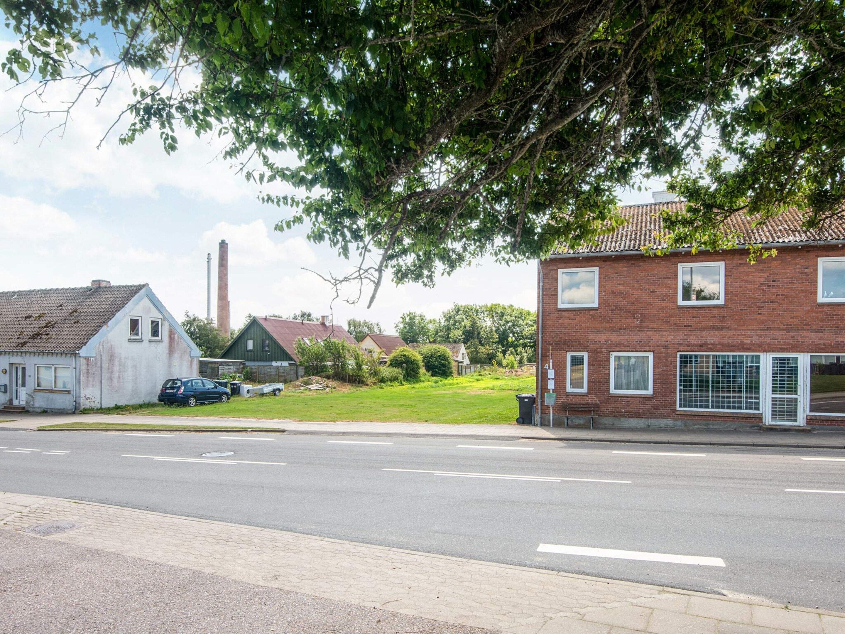 A street view with a brick house, a car, and a distant industrial chimney.